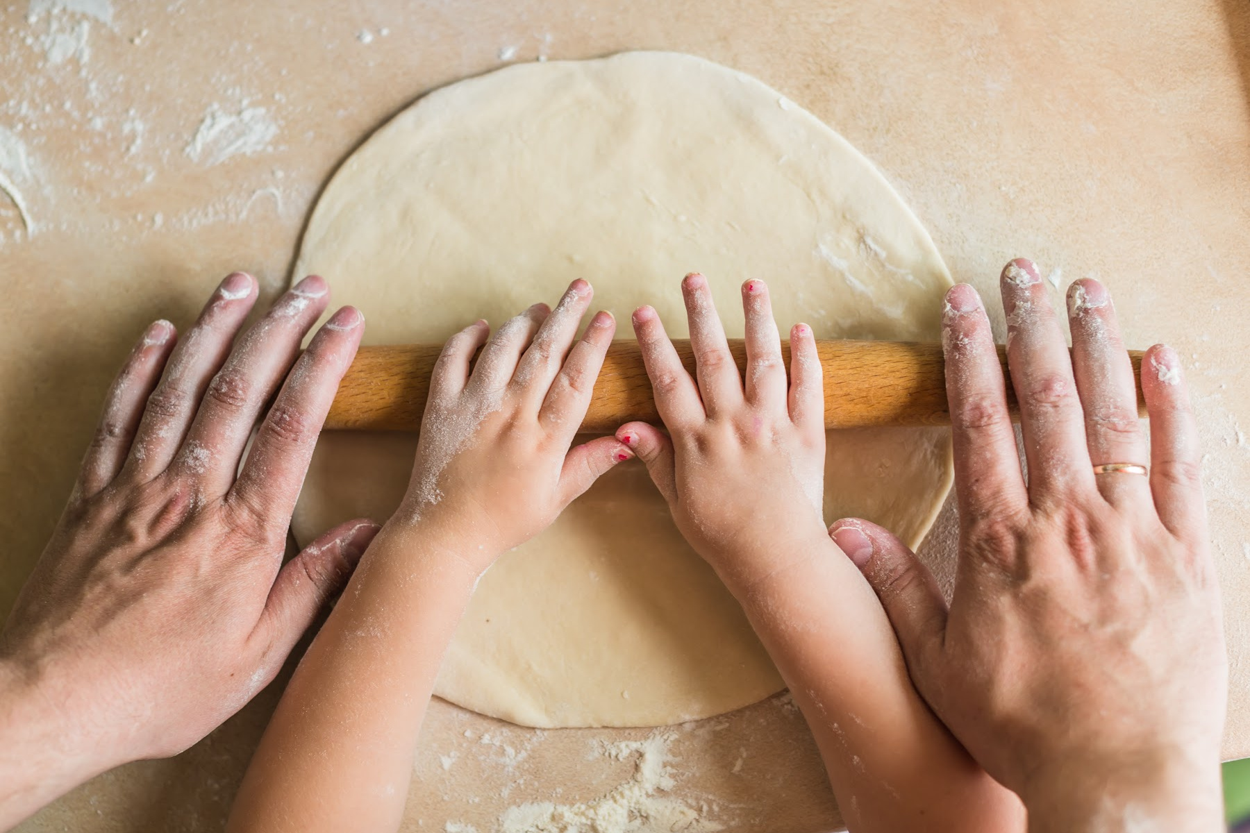 adult's and child's hands rolling out a pie crust together