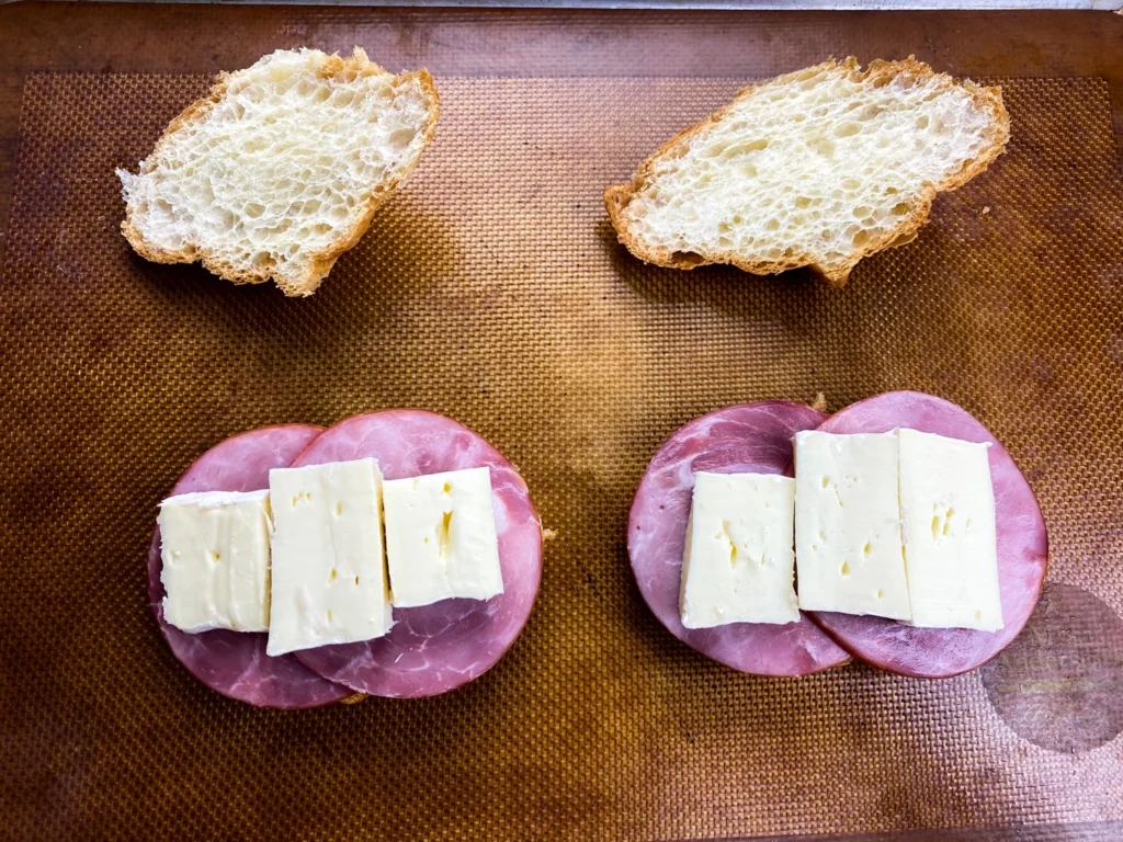 Brie cheese layered over ham on artisan bread before baking for warm croissant sandwiches.