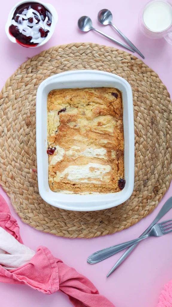Golden baked cherry dump cake in a white dish on pink background
