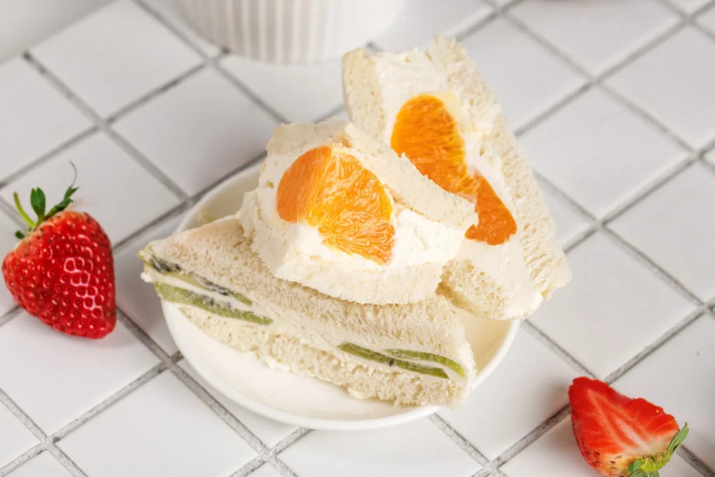 Assorted fruit sando sandwiches with strawberries, oranges, and kiwi displayed on plates.