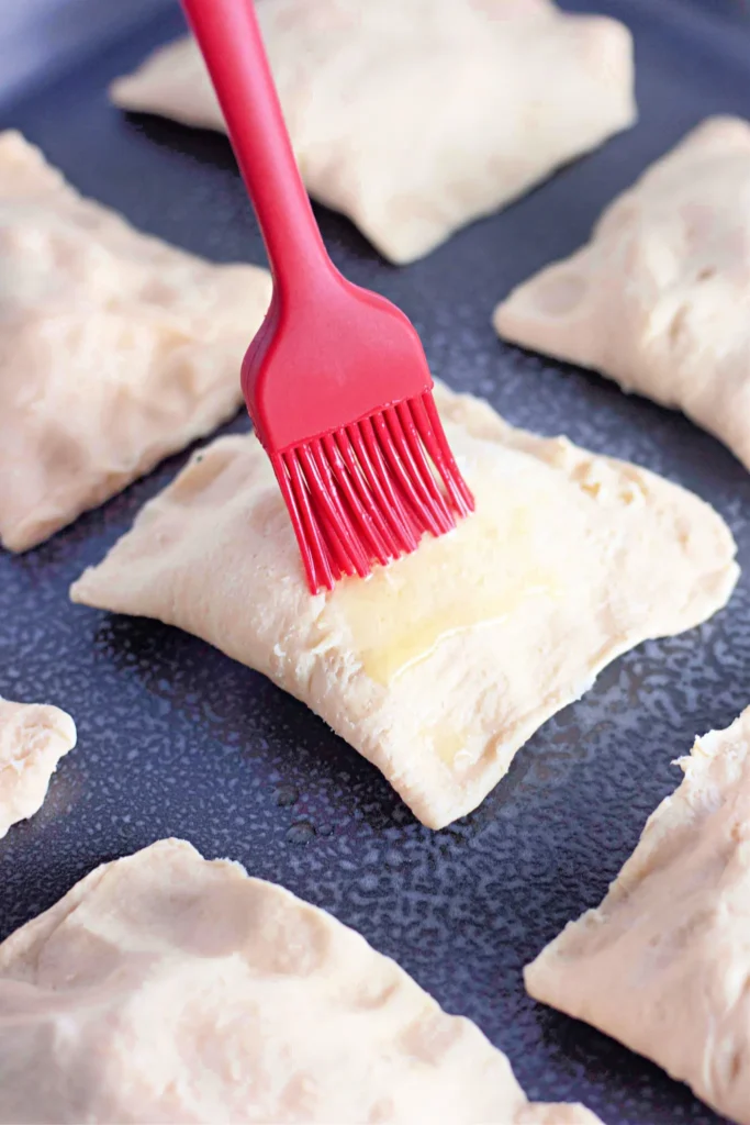 Unbaked chicken crescent pockets being brushed with melted butter before baking.