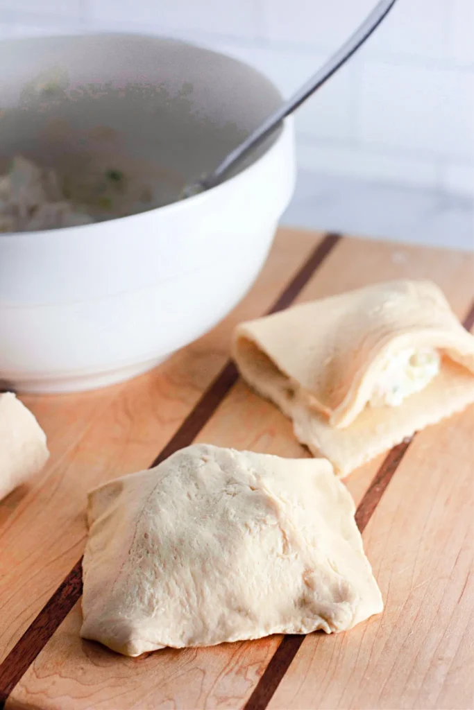 Crescent roll pockets folded over creamy chicken filling, ready to bake.
