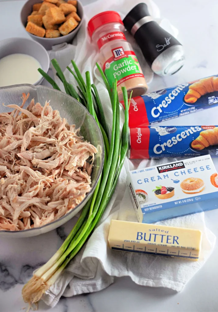 Ingredients for chicken crescent pockets including shredded chicken, crescent rolls, cream cheese, butter, and seasonings.