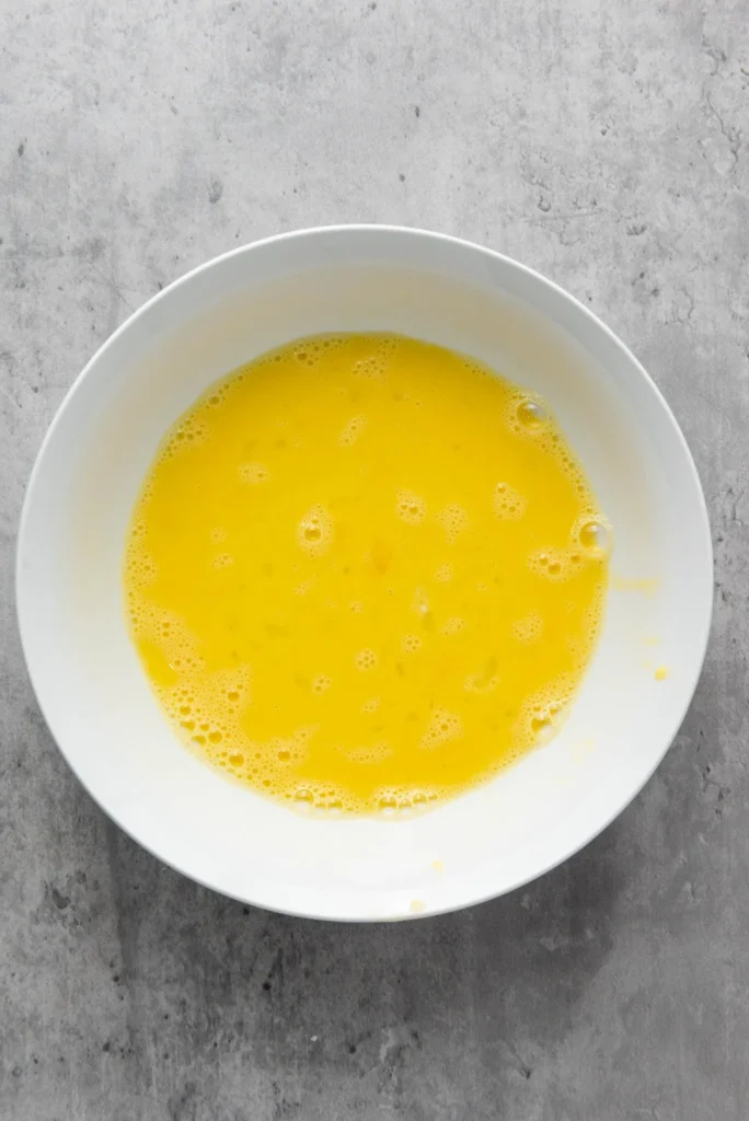 White bowl filled with whisked beaten eggs.