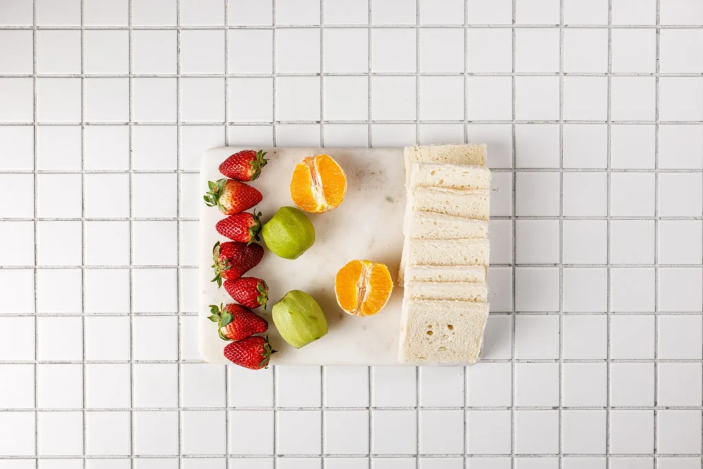 Fresh strawberries, kiwi, orange halves, and sliced bread prepared for fruit sandwiches.