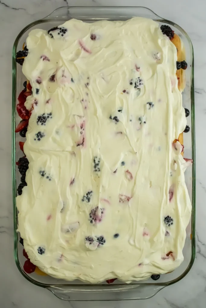 Final cream layer covering tiramisu in glass baking dish.