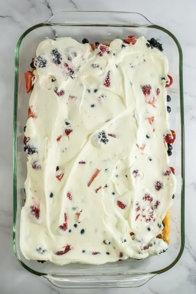 First layer of cream mixture spread over berries and ladyfingers in a glass dish.