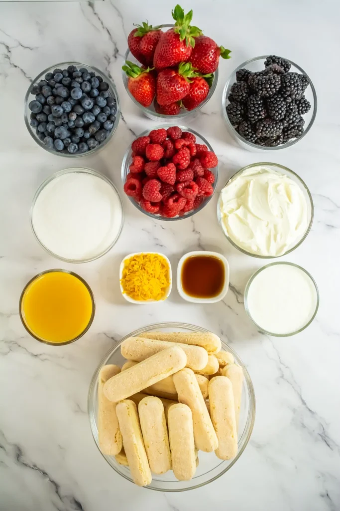 Overhead view of ingredients for mixed berry tiramisu, including ladyfingers, mascarpone, heavy cream, sugar, orange juice, zest, vanilla, and fresh berries.