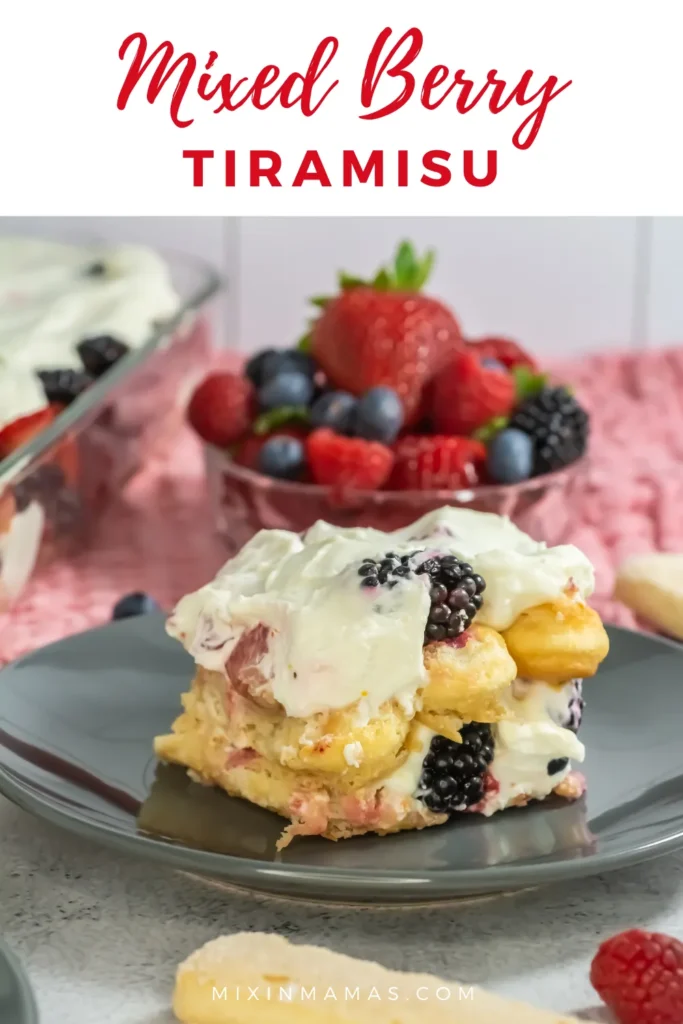 Slice of no-bake mixed berry tiramisu on a gray plate with fresh strawberries, blueberries, blackberries, and raspberries in the background.
