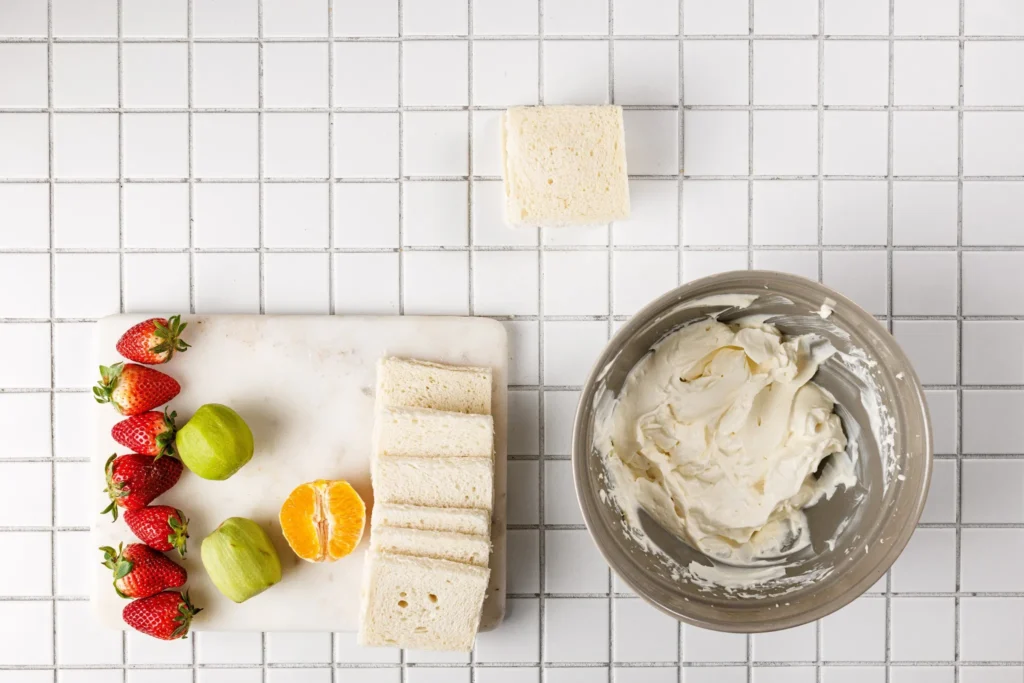 Fruit sandwich being layered with whipped cream and fruit slices before sealing.