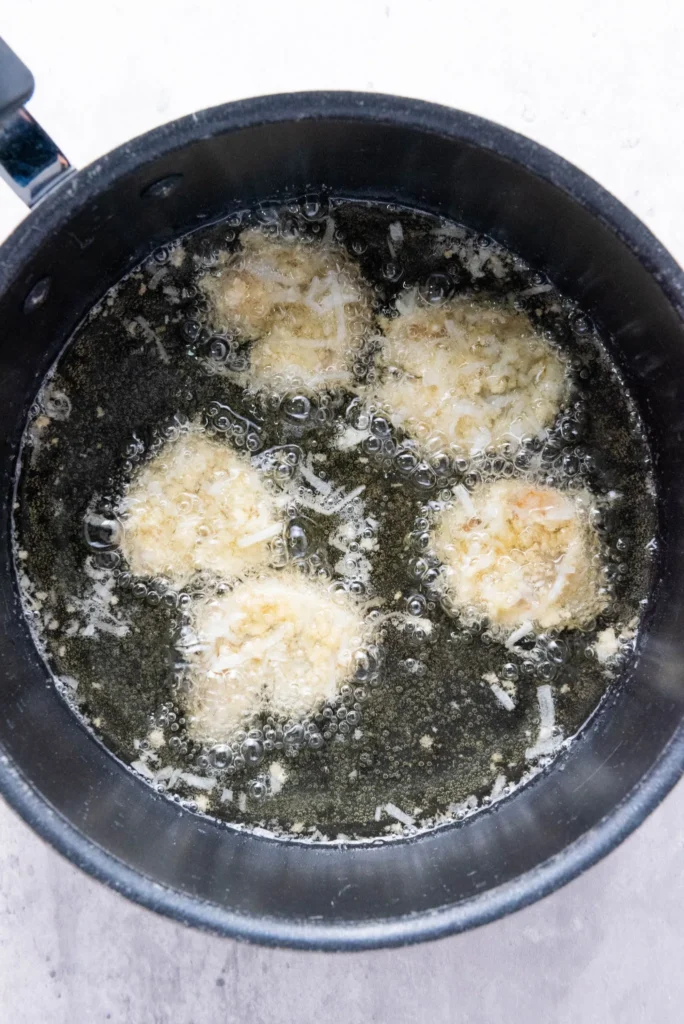 Coconut shrimp sizzling in hot oil in a saucepan.