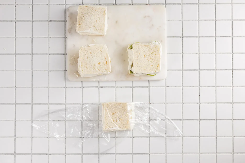 Fruit sando sandwich being wrapped tightly in plastic wrap before chilling.