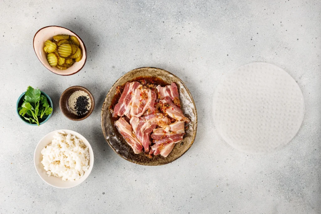 Pork belly marinating in soy sauce, ginger, garlic, and chili paste on a platter surrounded by other roll ingredients.