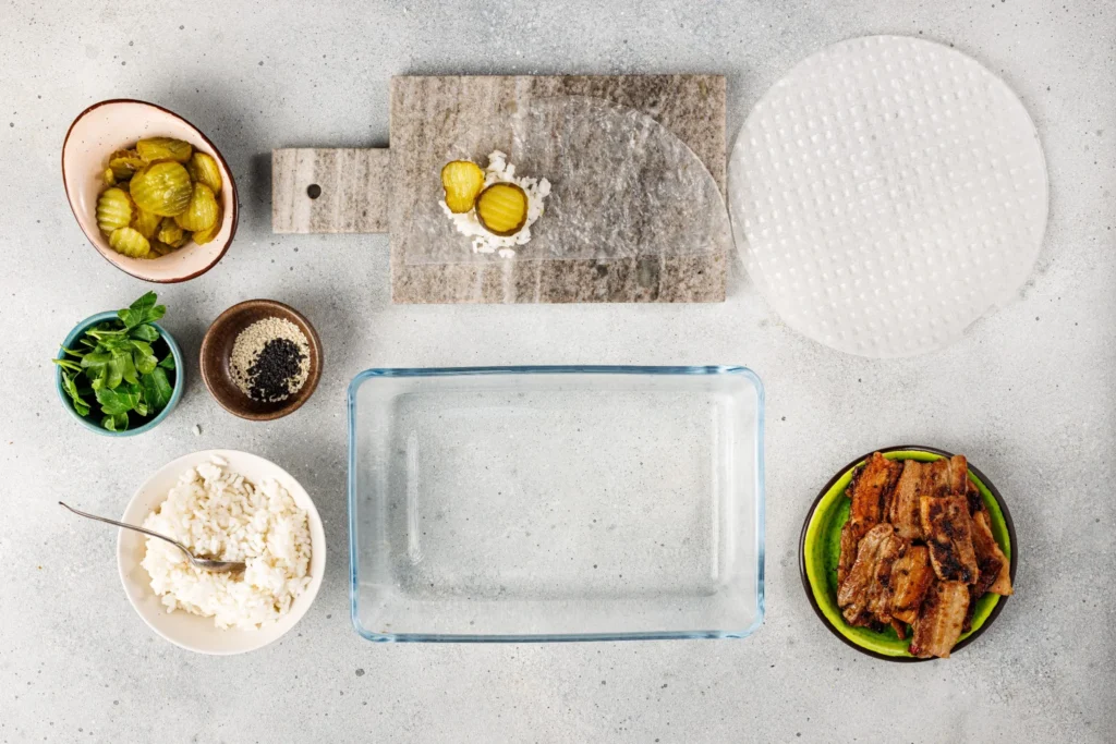 Step showing sliced pickled cucumbers added on top of rice in rice paper wrapper.