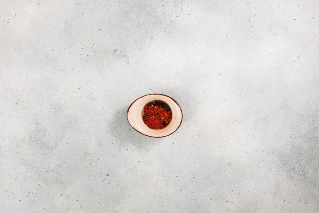 Small bowl of soy sauce marinade with red chili and garlic for spicy pork belly hand rolls.
