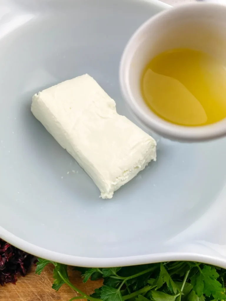 Pouring fresh orange juice into a bowl with softened cream cheese to start the cheese ball mixture.