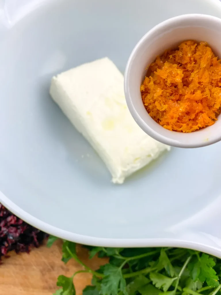 Adding bright orange zest to a bowl of cream cheese for citrus flavor.