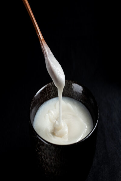 A bowl containing partially solidified lard, with a wooden spoon scooping some out, set against a black background.