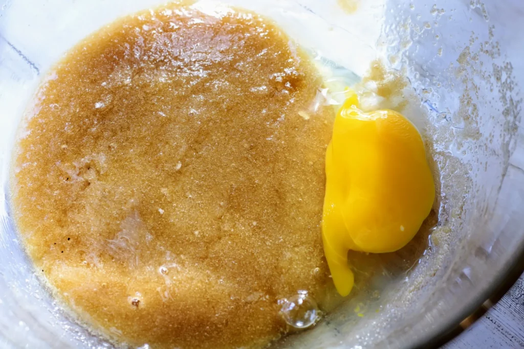 An egg cracked into the bowl of mixed butter and sugar, ready to be stirred in.