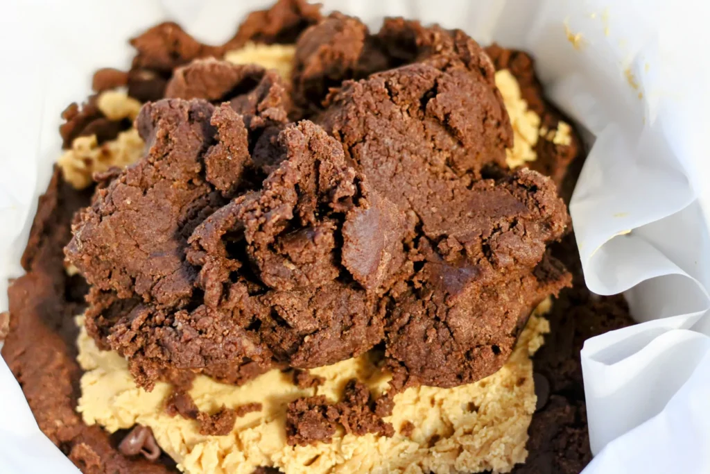 Chocolate cookie dough being added on top of the peanut butter layer.
