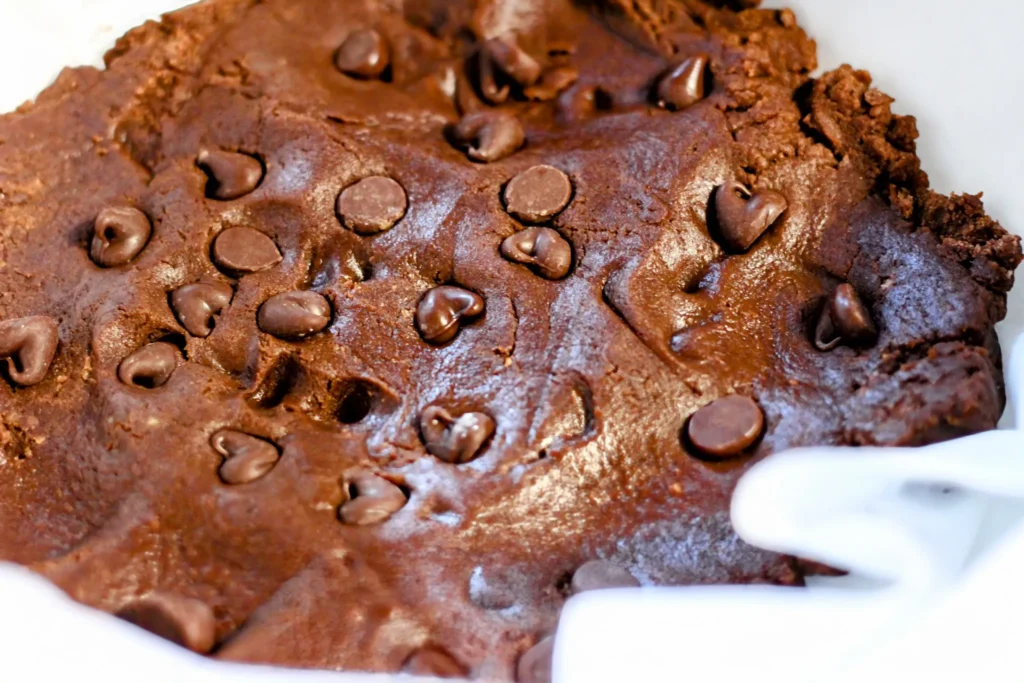The bottom layer of chocolate cookie dough pressed into a lined baking pan with chocolate chips sprinkled on top.