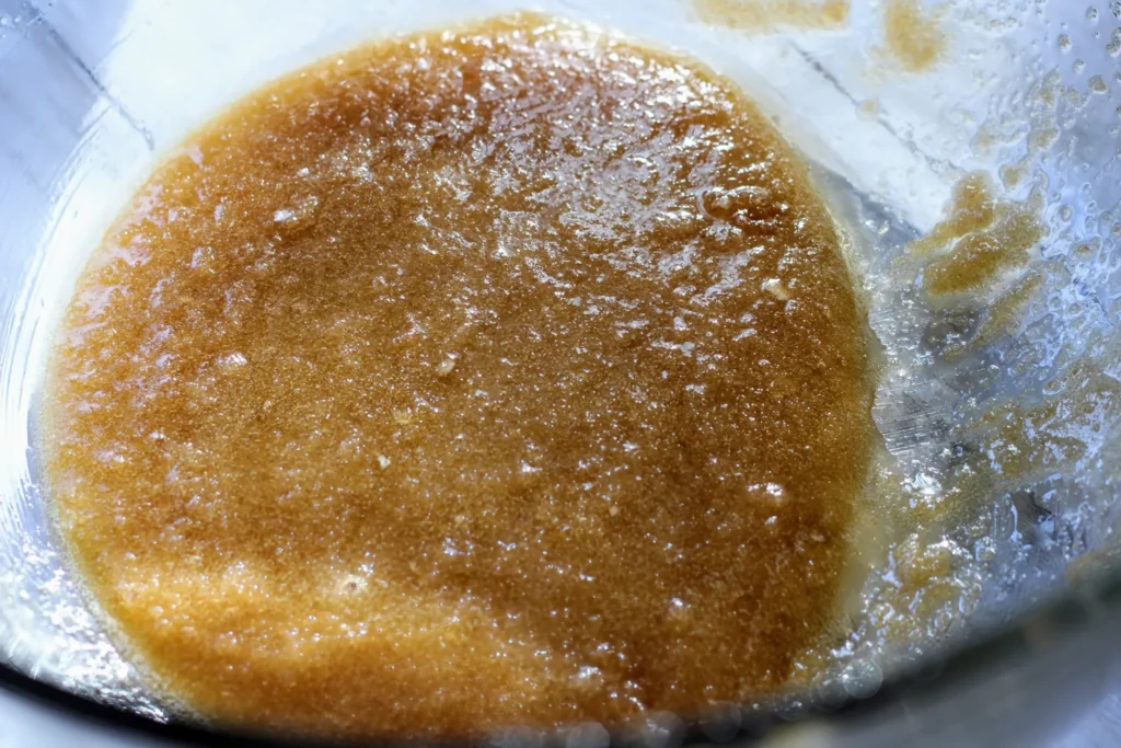 Butter and sugars fully stirred into a smooth mixture in a clear mixing bowl.