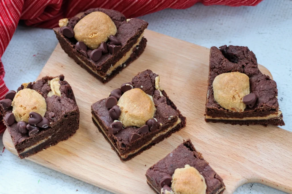 Several Buckeye Cookie Bars displayed on a wooden cutting board, showing the layered peanut butter center.