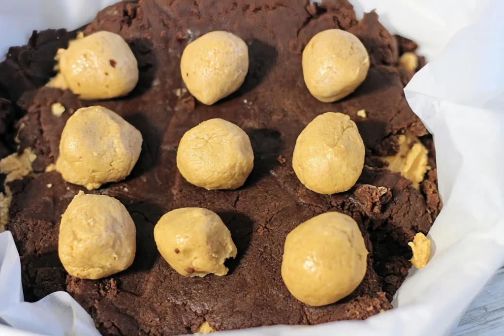 Small peanut butter balls arranged on top of the unbaked cookie bar layer.