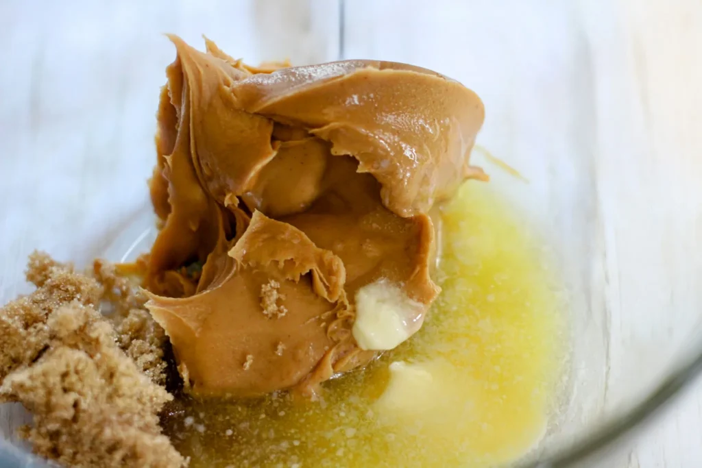 Peanut butter, melted butter, and brown sugar in a mixing bowl before stirring.