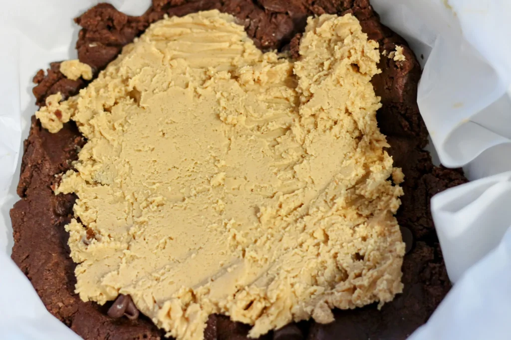 Peanut butter filling spread evenly over the bottom chocolate cookie dough layer in the baking pan.