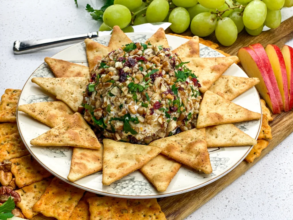 Finished orange cranberry cheese ball surrounded by crackers, apple slices, and grapes on a serving board.