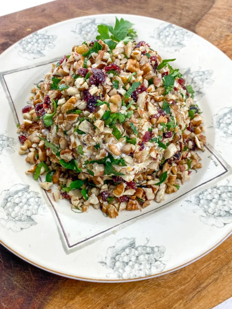 Close-up of festive orange cranberry cheese ball coated in pecans and parsley on a vintage plate.