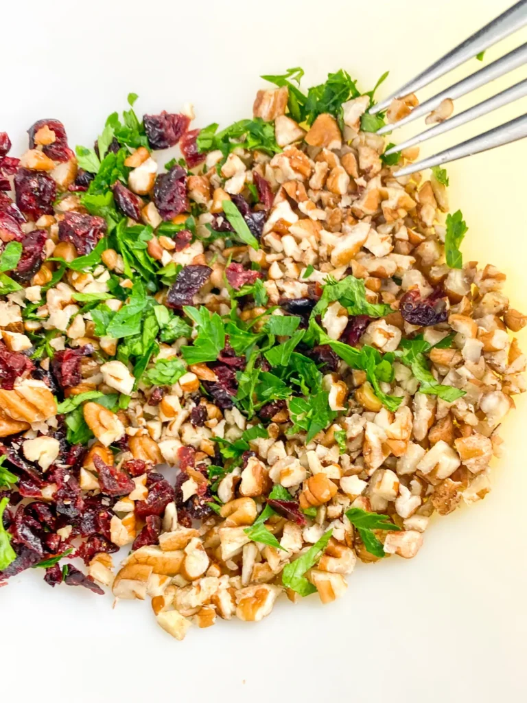 Fork mixing chopped pecans, cranberries, and parsley together in a bowl for cheese ball coating.