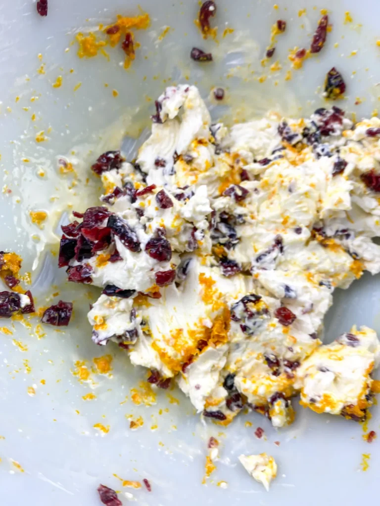 Stirring together cream cheese, orange zest, and dried cranberries to form the cheese ball base.