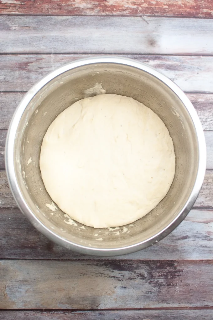 Dough in a metal bowl after rising, smooth and doubled in size.