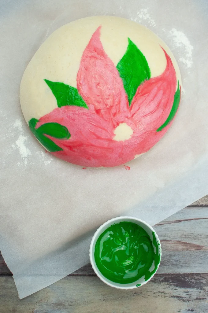 Green leaves being painted around the red poinsettia petals on the dough surface.