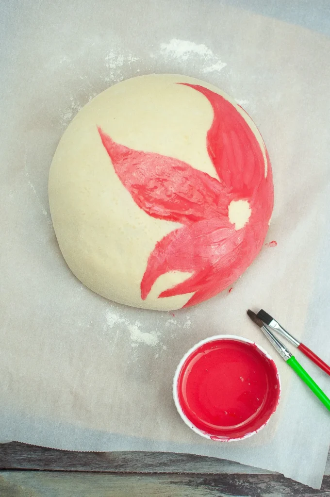Loaf being painted with the first layer of red poinsettia petals using small paintbrushes.