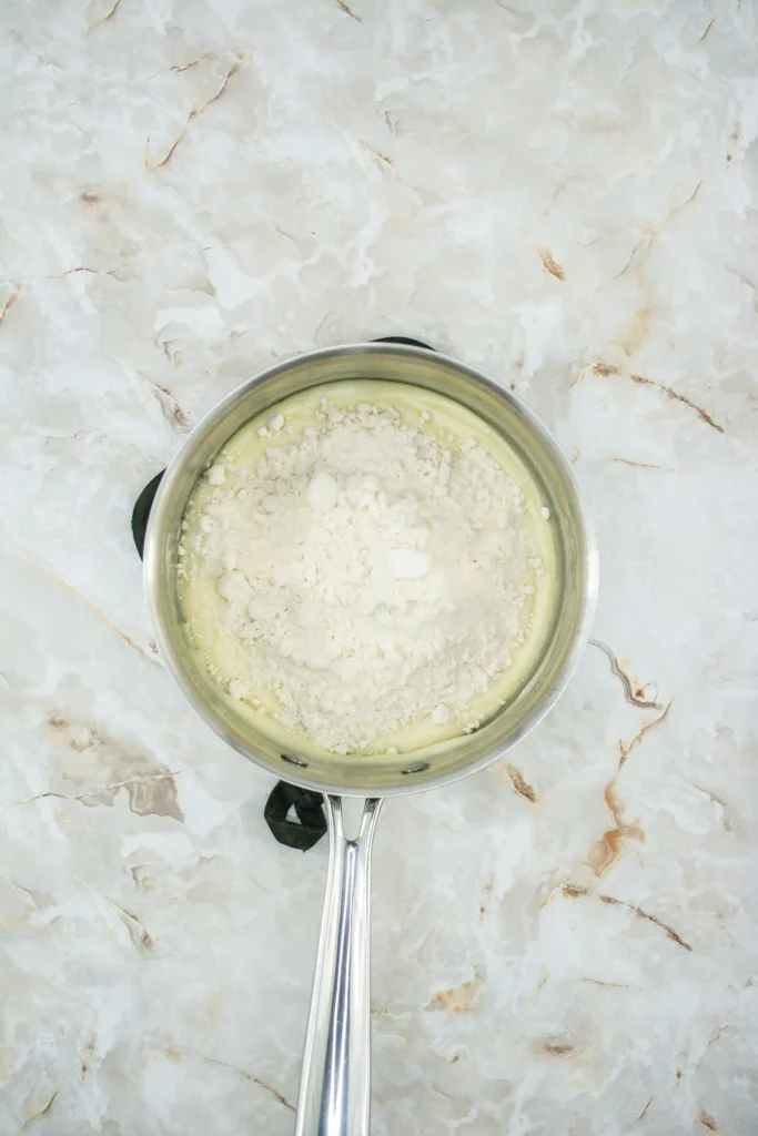 Sugar cookie mix poured into melted white chocolate and condensed milk mixture in saucepan.