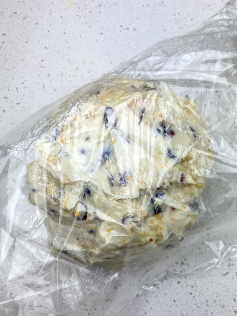 Shaping and wrapping the orange cranberry cheese ball tightly in plastic wrap before chilling.