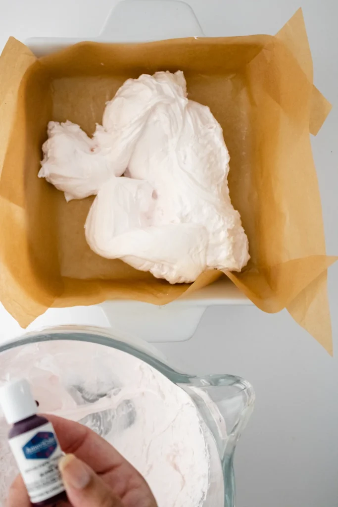 Spoonfuls of marshmallow mixture added to lined baking pan