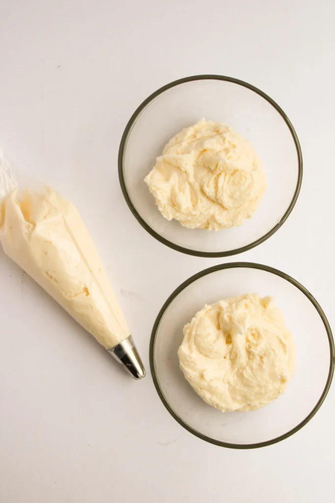 Plain buttercream frosting divided into bowls with piping bag ready for coloring