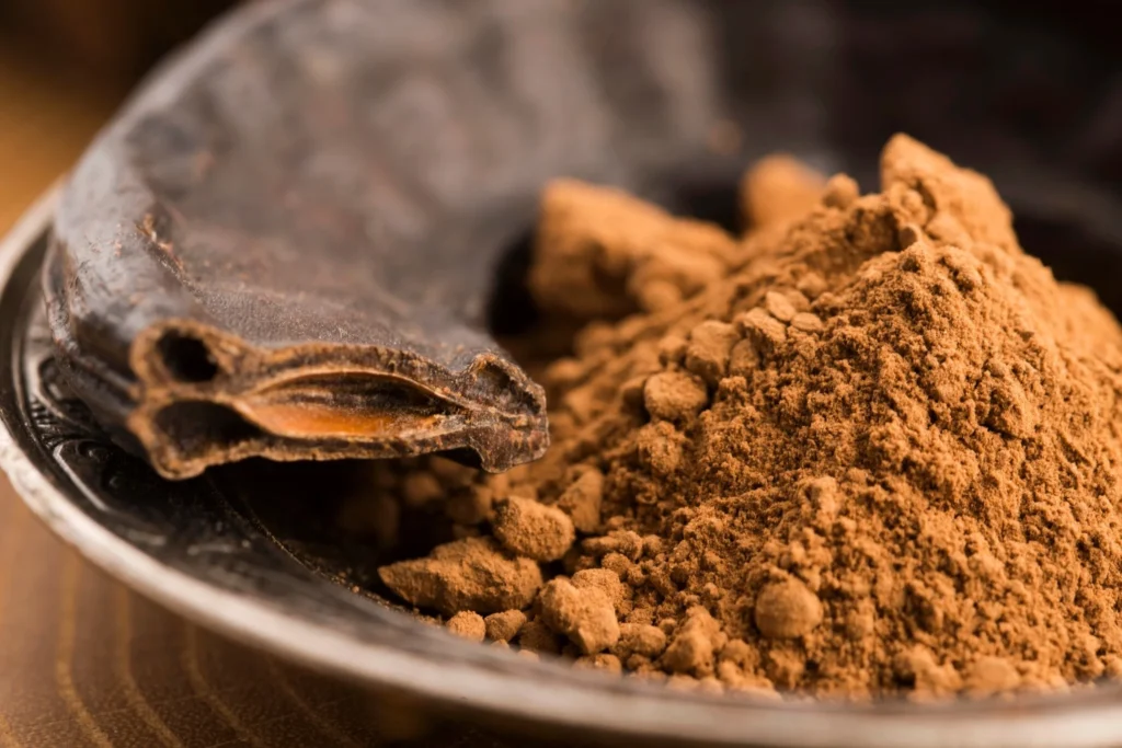 Ground carob powder with whole dried carob pods in a metal dish