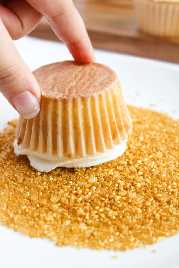 Pressing a cupcake into gold sanding sugar to create a Christmas ornament look
