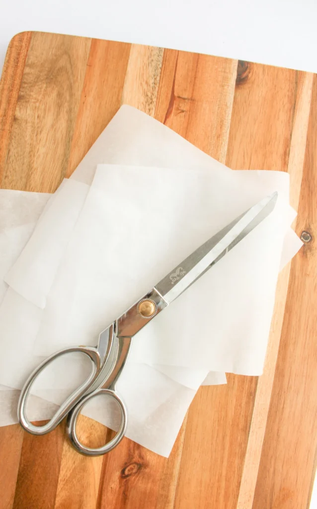 Scissors and parchment paper used to prepare cupcakes for Christmas ornament decorating