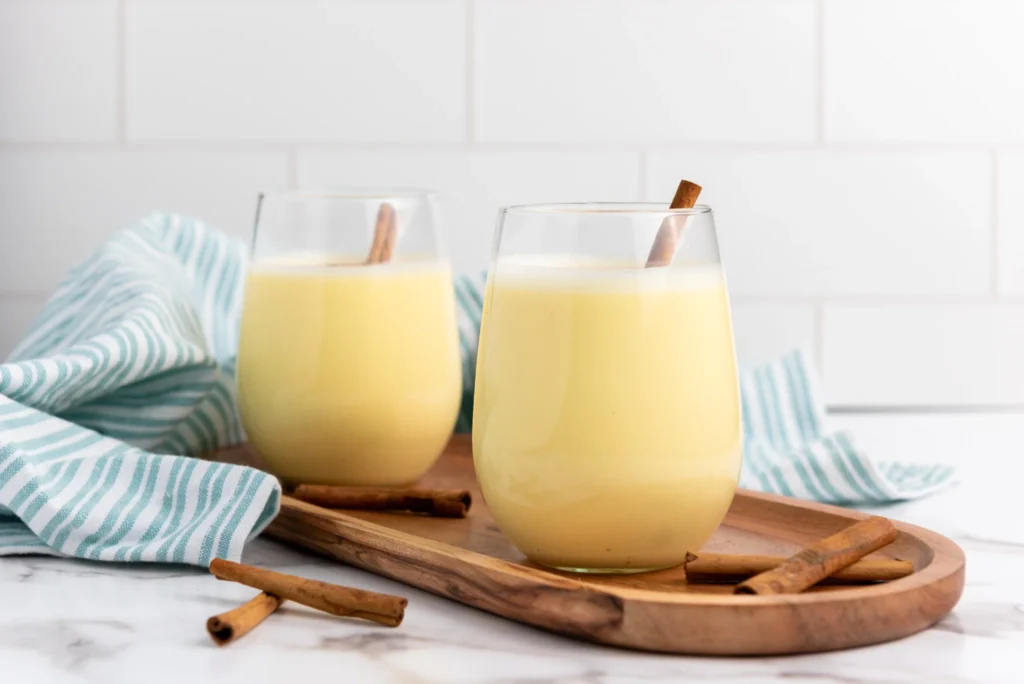 Two glasses of homemade eggnog garnished with cinnamon sticks