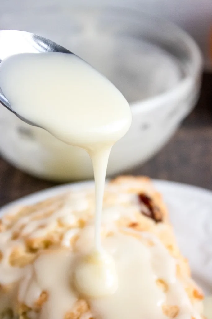 Close-up of orange glaze being poured over an orange cranberry scone