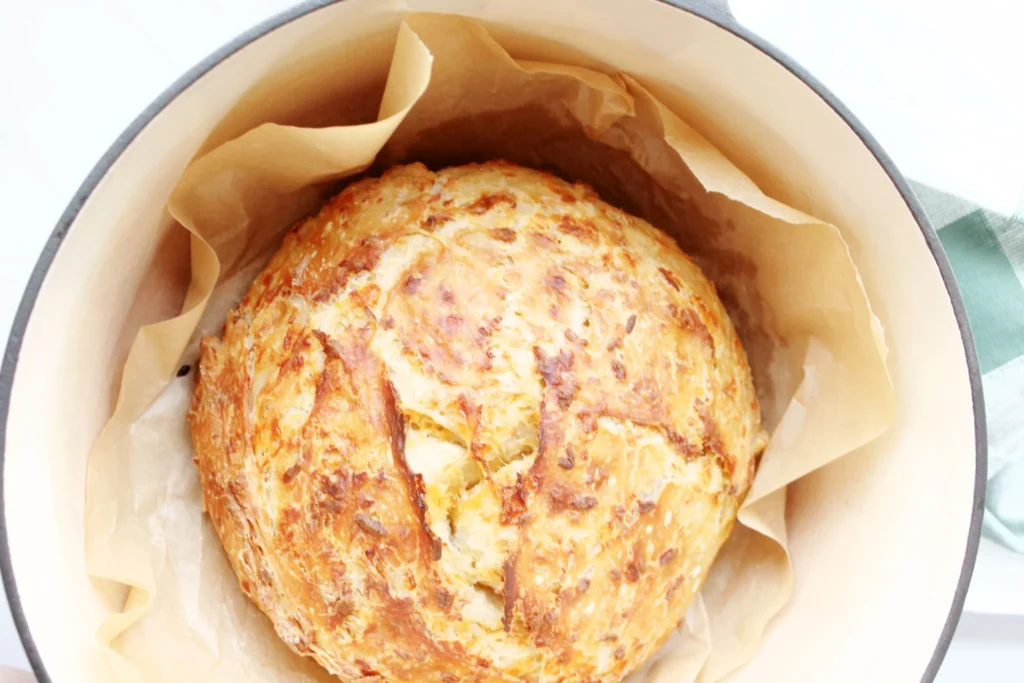 Golden baked no-knead cheddar bread loaf in Dutch oven