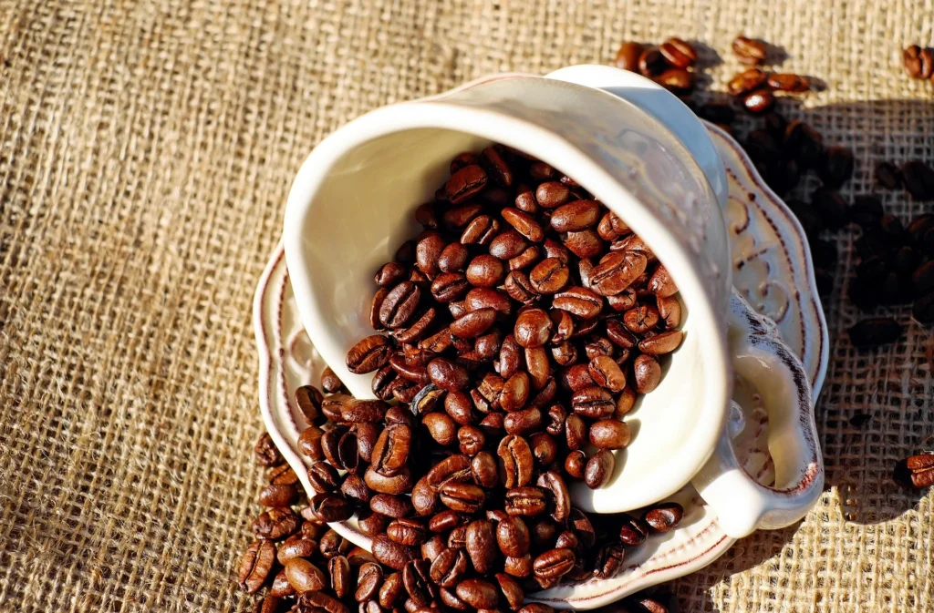 Roasted coffee beans spilling out of a white cup onto a burlap surface