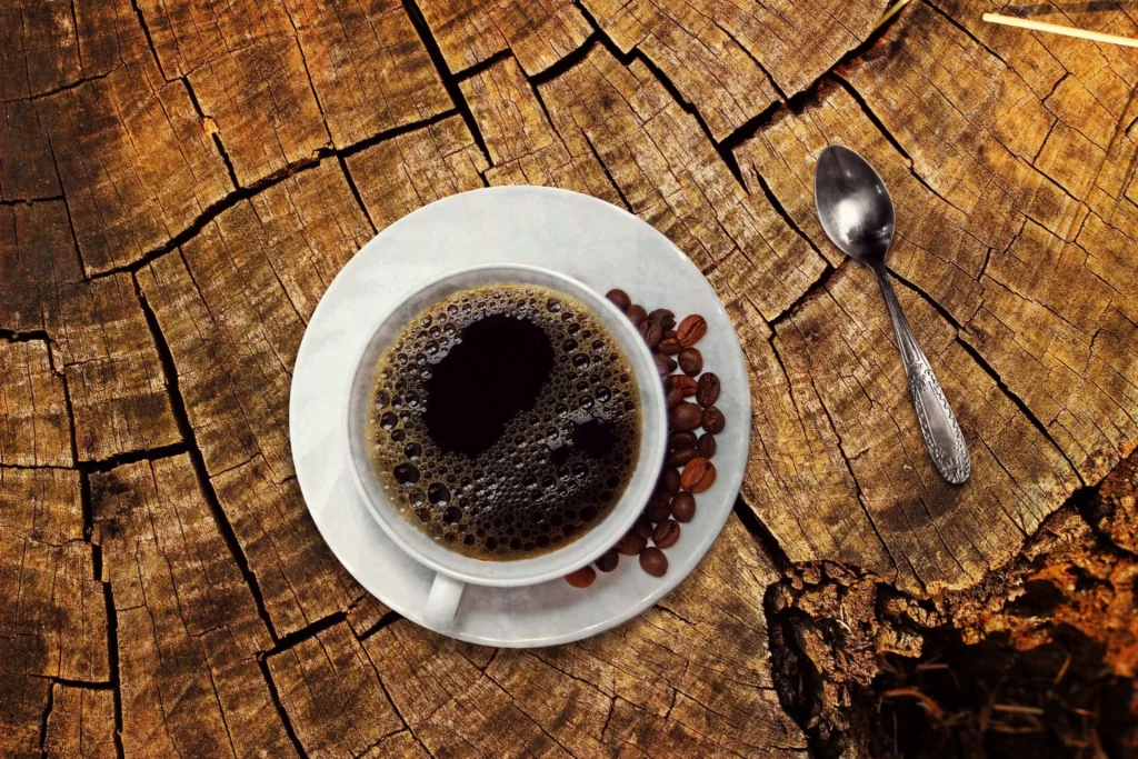 Cup of black coffee on a rustic wooden surface with scattered coffee beans and a spoon