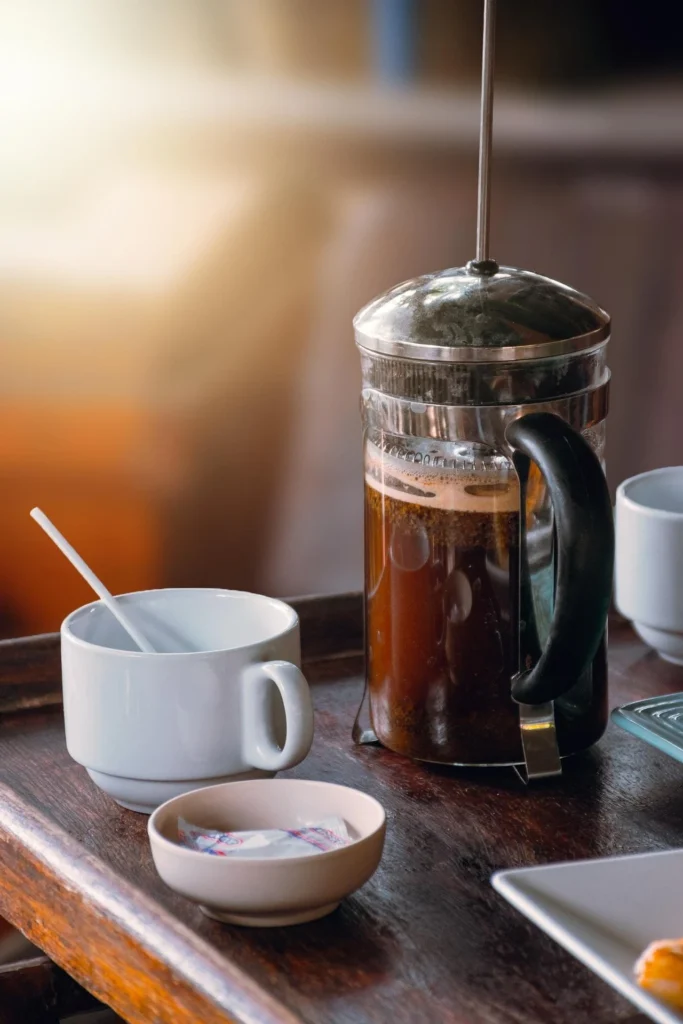 French press coffee brewing on a wooden table beside a white mug